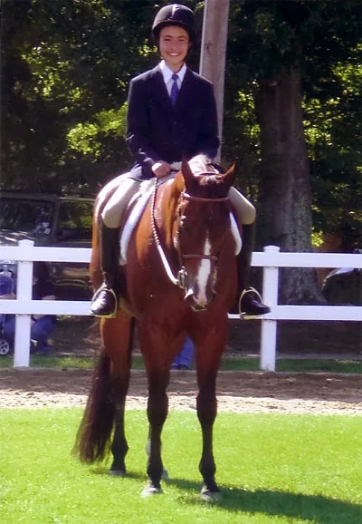 A rider on a chestnut horse beside a white fence
